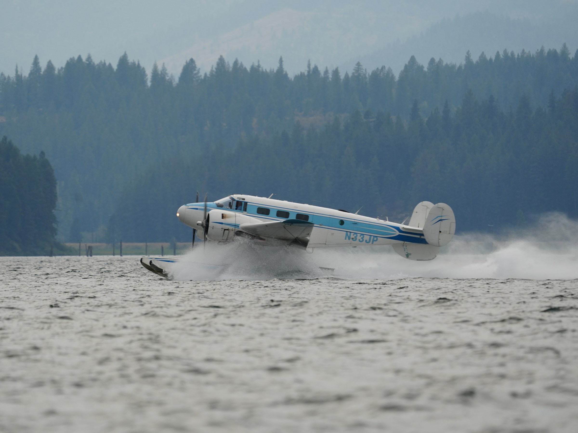 Seaplane taking off from water with forested hills in the background.