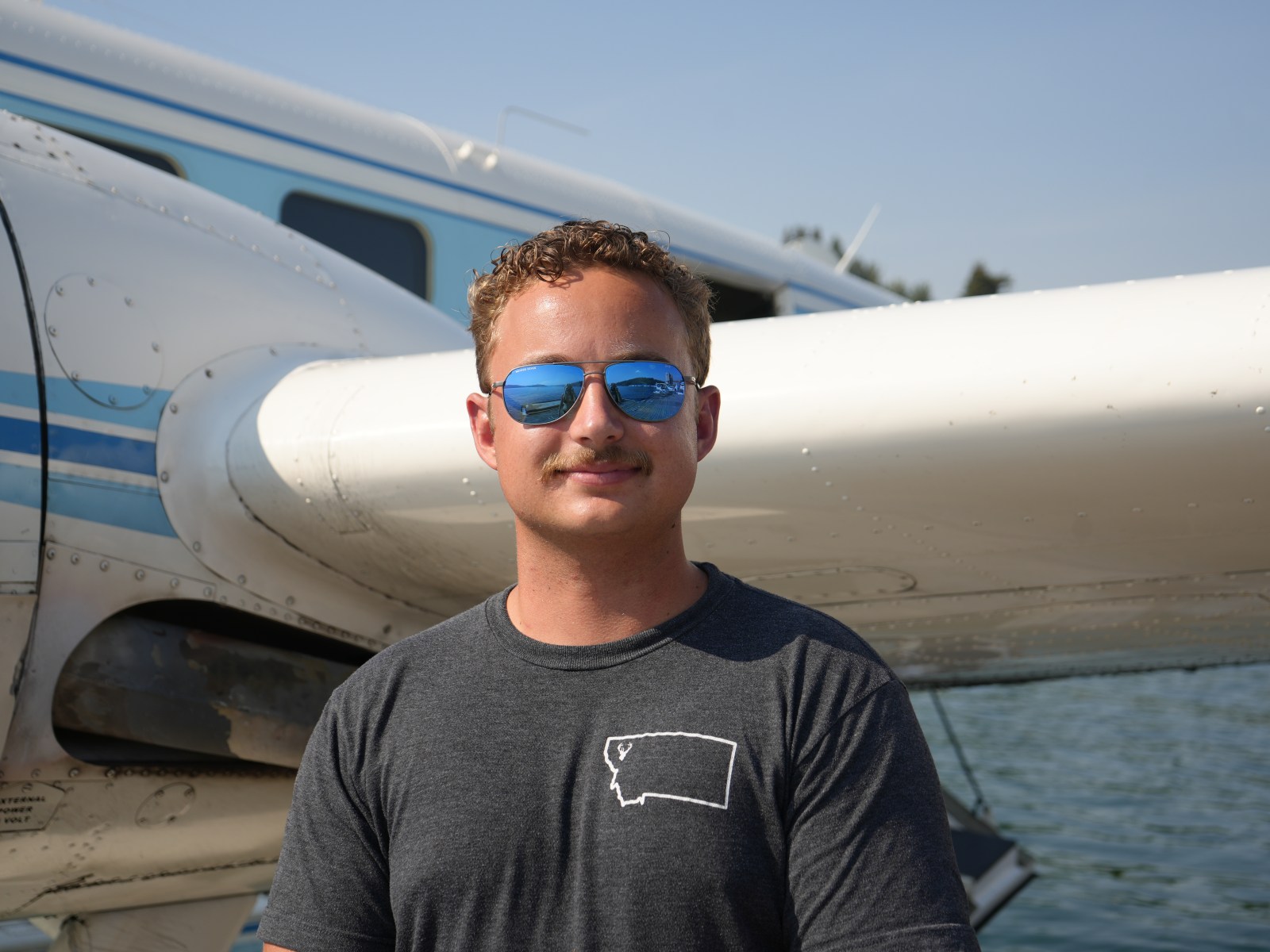 Man in sunglasses standing by a small aircraft on a sunny day.