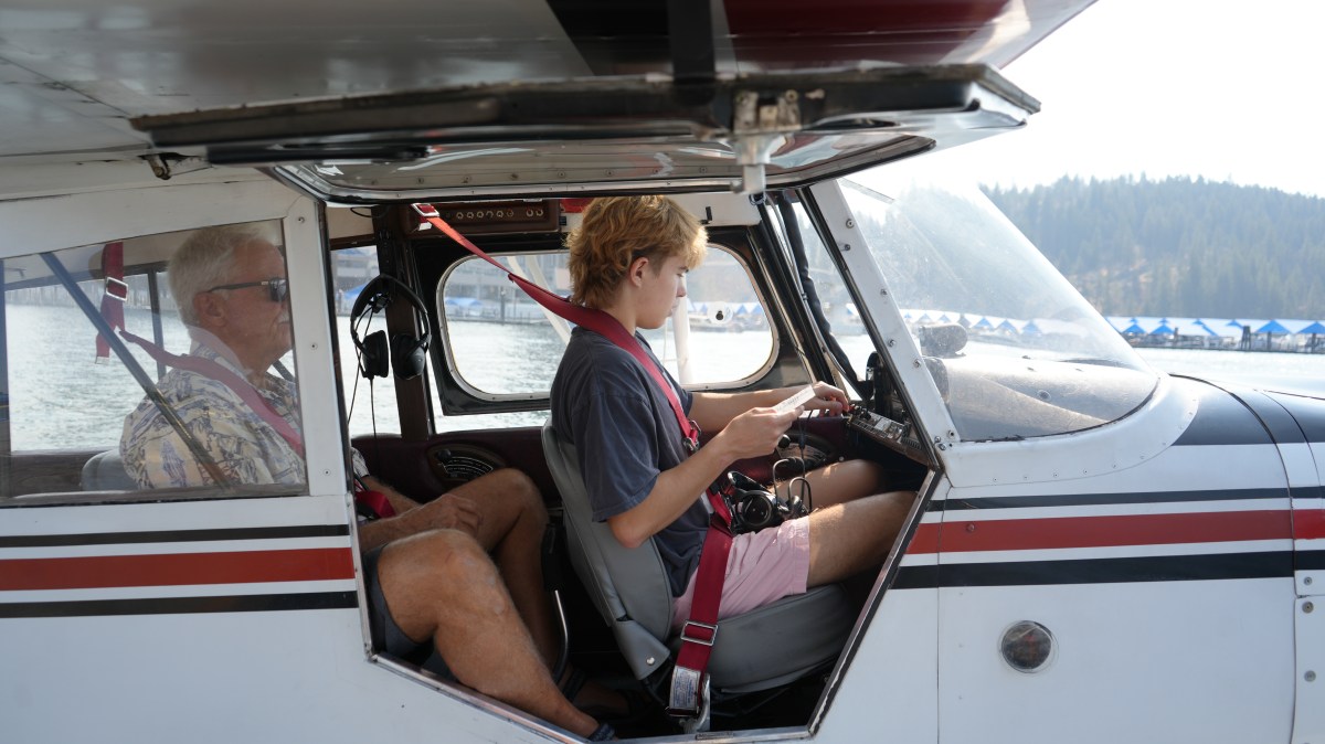 Two people seated in a small aircraft near a body of water.